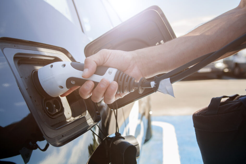 Hand hält E-Ladestecker und steckt dieses in schwarzes Auto