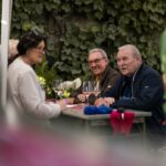 zwei ältere Paare unterhalten sich lachend mit Wein an einer Bierbank in den Weinbergen