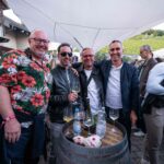 vier lachende Männer mit Brille oder Sonnenbrille vor Weinfass mit Wein beim Kundenevent der WVV