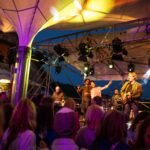 Liveband am Abend auf der Bühne in den Weinbergen umgeben von Menschen und Lichtern