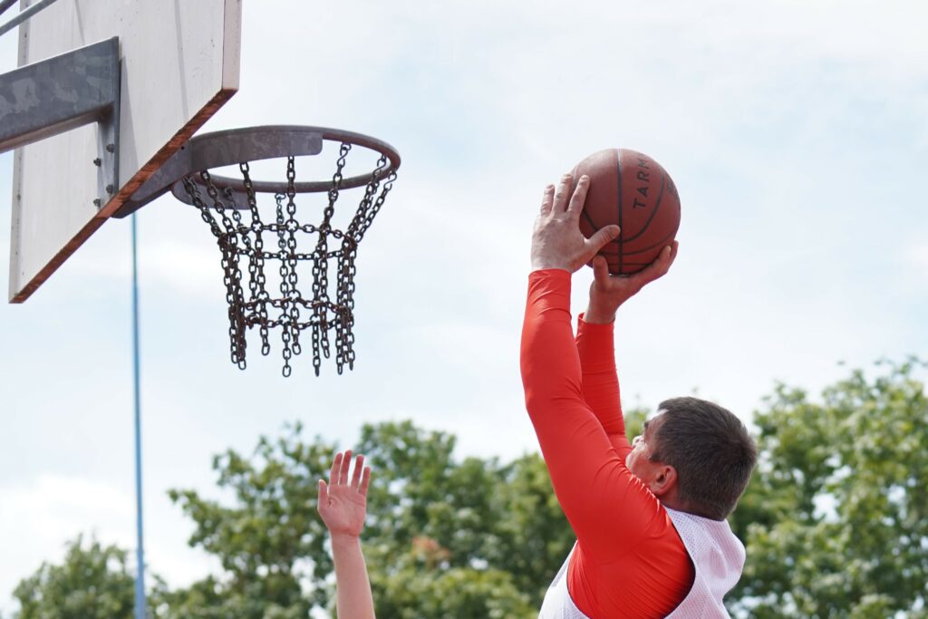 WVV Jugendstreetballturnier: Mann mit rotem Langarmshirt wirft unter freiem Himmel mit einem Basketball auf den Korb