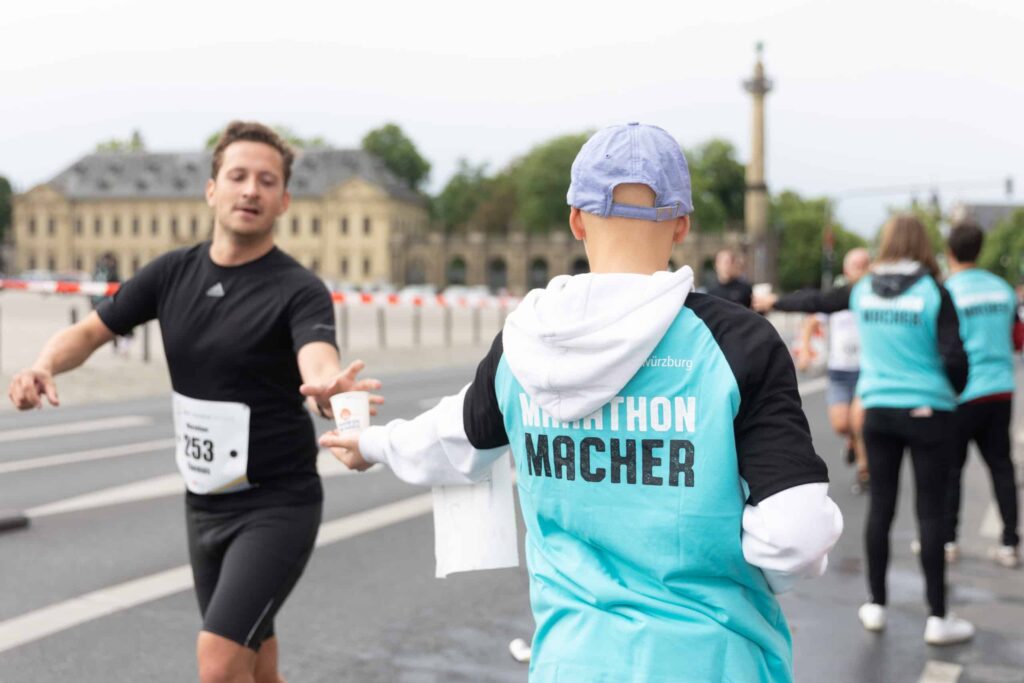 Ehrenamtliche Marathon-Helfer reichen den Läufer/innen Wasserbecher.