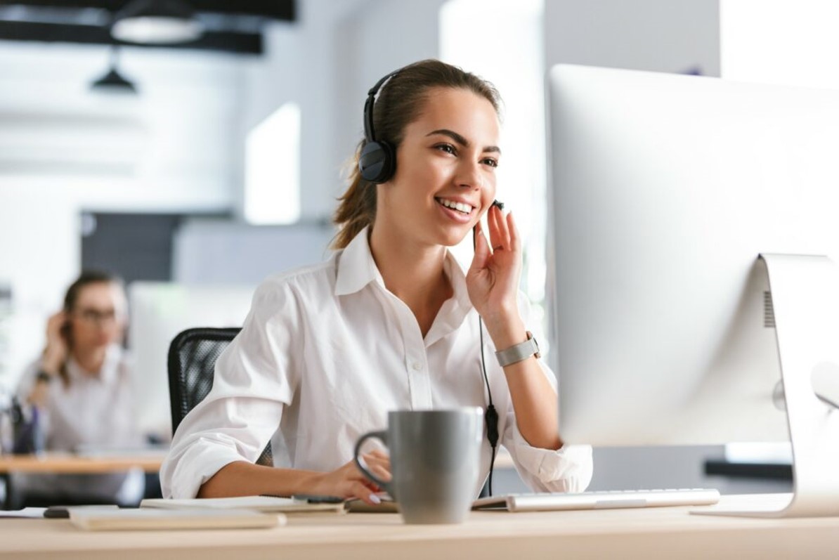 lachende Frau im telefonischen Hotlineservice mit Headset vor dem PC