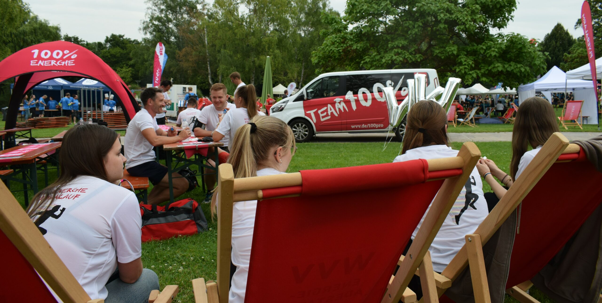 sitzende Mitarbeiter der WVV beim Firmenlauf 2024 im Hintergrund der Bus mit Team 100%