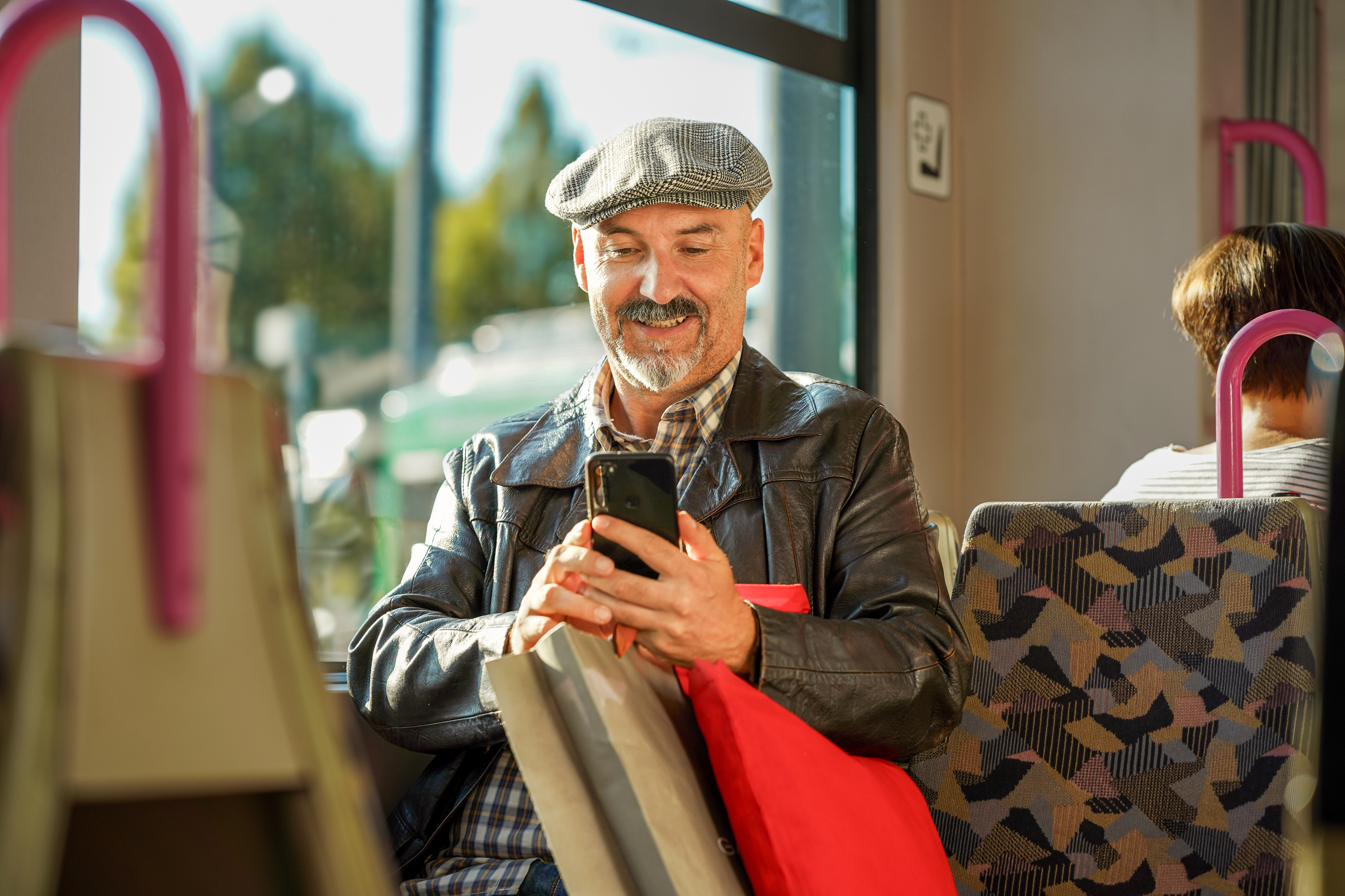 Älterer Herr sitzt in der Würzburger Straßenbahn mit seinem Smartphone in der Hand