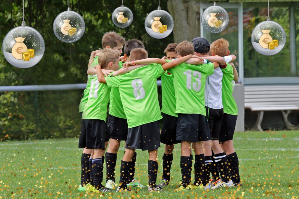 Jugend-Fußballer stehen Arm in Arm und zeigen Zusammenhalt. Über ihnen hängen mit Geldsäcken versehene Schneekugeln an Schnüren herunter